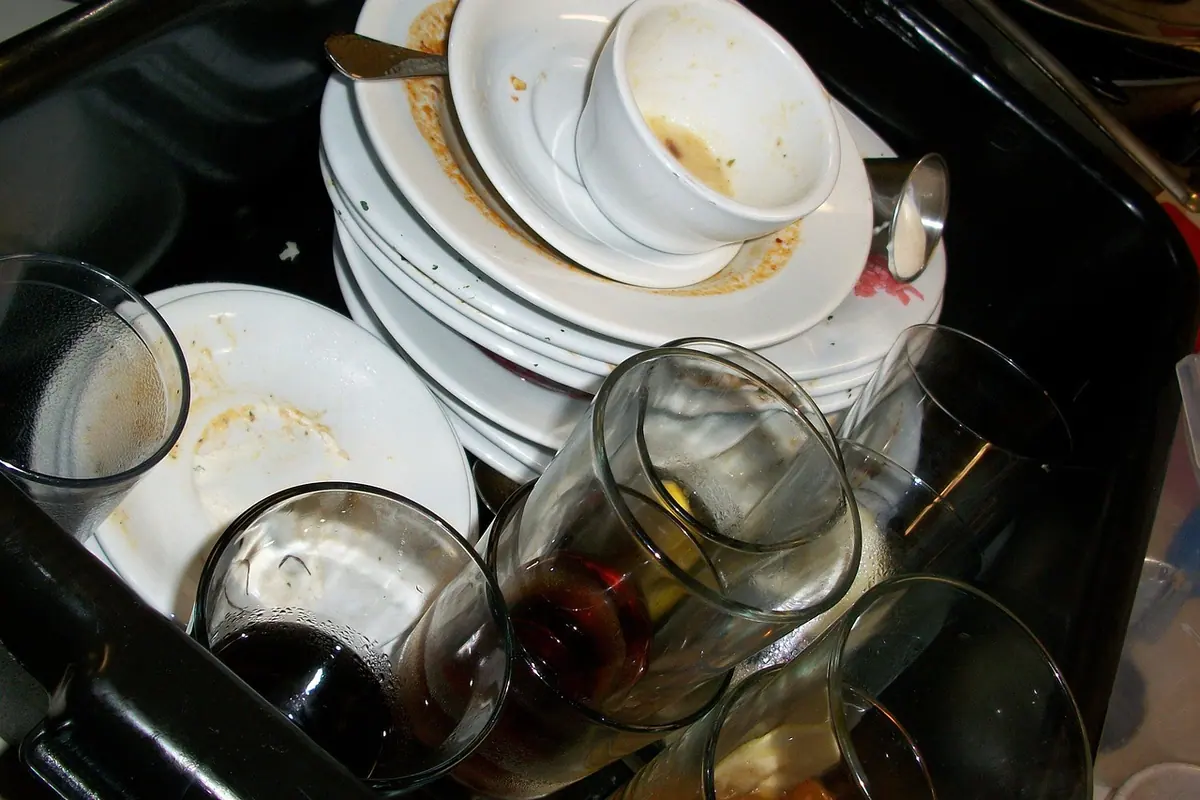 Fregadero lleno de platos y vasos sucios con restos de comida