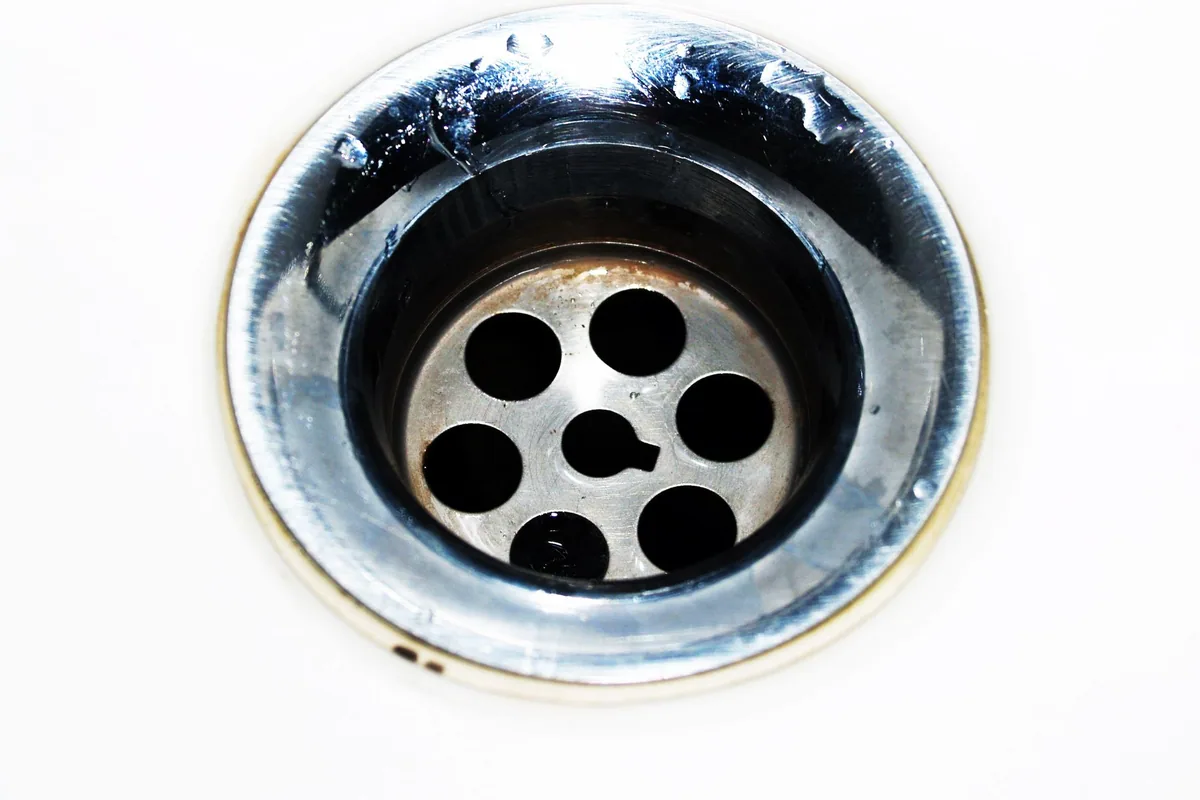 Desagüe cromado de un lavabo con su rejilla de agujeros y gotas de agua