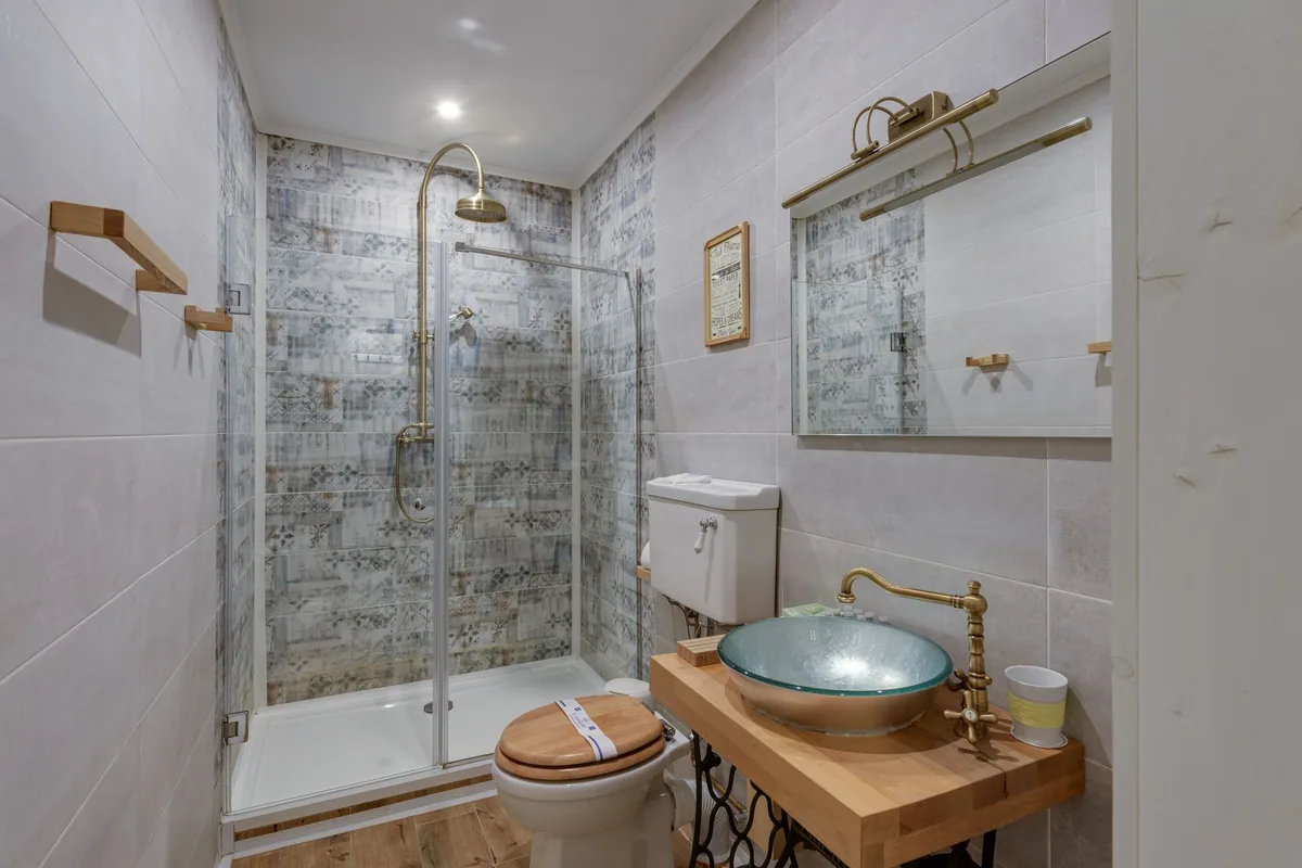 Baño pequeño de apartamento turístico con ducha de mampara, inodoro y lavabo sobre una encimera de madera