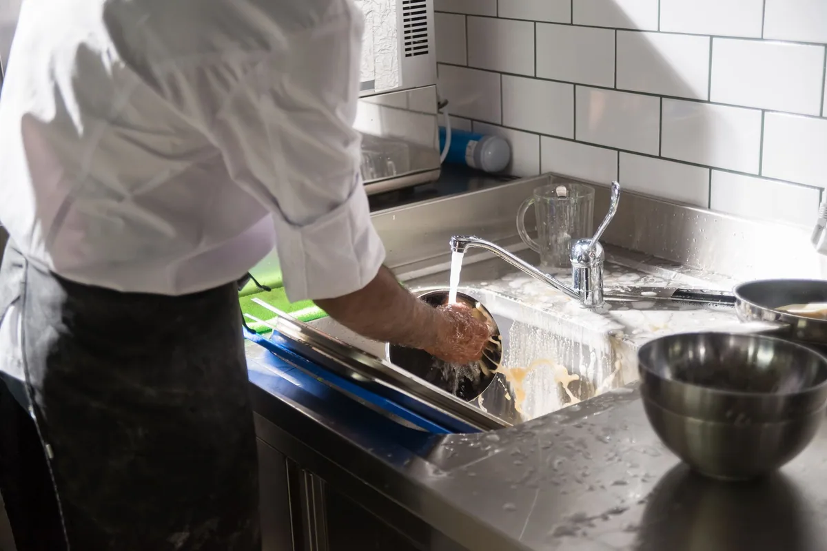 Cocinero de espaldas fregando en el fregadero de acero inoxidable de la cocina de un restaurante