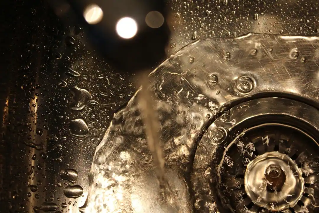 Chorro de agua cayendo sobre el desagüe de un fregadero de acero inoxidable