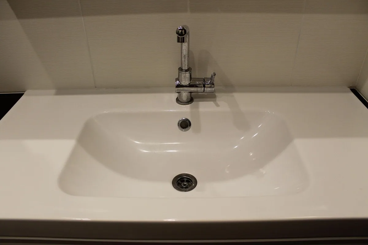 Lavabo blanco con su desagüe y el rebosadero, bajo un grifo monomando